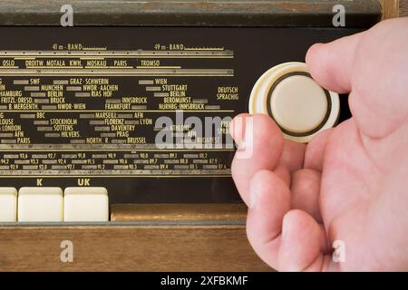 Autentica vecchia radio degli anni '60. Vista frontale. Su sfondo bianco. Tracce di tempo. La mano di un uomo sulla manopola radio che imposta le onde. Primo piano Foto Stock