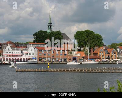 Veduta di un porto con vari edifici e di una chiesa sullo sfondo su un cielo nuvoloso, Kappeln, schlewsig-holstein, germania Foto Stock