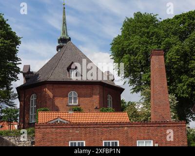 Edificio in mattoni rossi con torre della chiesa e albero contro un cielo nuvoloso, Kappeln, Schlewsig-holstein, germania Foto Stock