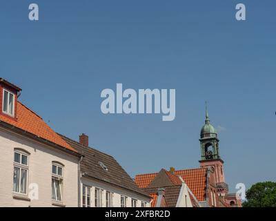 Vista della torre di una chiesa e degli edifici vicini con tetti arancioni sotto un cielo limpido, friedrichstadt, schleswig-holstein, germania Foto Stock