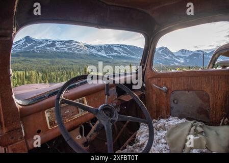 Vecchio camion d'epoca arrugginito, annidato nella natura selvaggia con sfondo montano estivo. Foto Stock