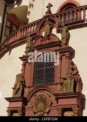 Vista dettagliata della facciata della chiesa con decorazioni rosse e statue di santi che circondano la finestra, wuerzburg, baviera, germania Foto Stock