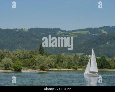 Barca a vela in un lago calmo con verdi coste collinari sullo sfondo, lindau, baviera, germania Foto Stock