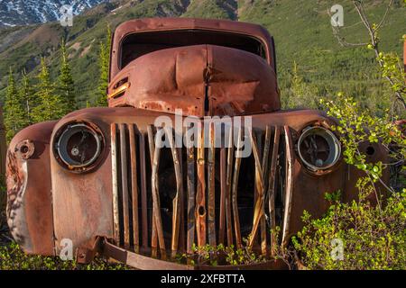 Vecchio camion d'epoca arrugginito, annidato nella natura selvaggia con sfondo montano estivo. Imbocca North Canol Road nel nord del Canada Foto Stock