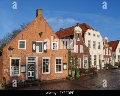 Case tradizionali con tetti di tegole rosse e strade acciottolate sotto un cielo azzurro, Greetsiel, Frisia orientale, Germania Foto Stock