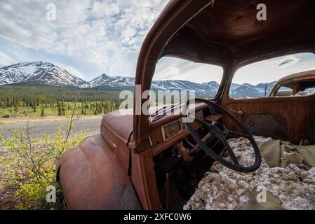 Vecchio camion d'epoca arrugginito, annidato nella natura selvaggia con sfondo montano estivo. Imbocca North Canol Road nel nord del Canada Foto Stock