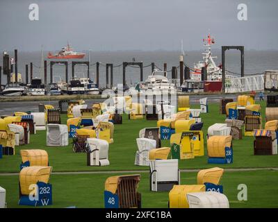 Diverse sedie colorate da spiaggia su un prato verde al porto con barche e navi, cielo nuvoloso sopra, cuxhaven, germania Foto Stock