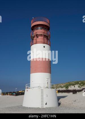 Un faro rosso e bianco si erge impensabilmente su una spiaggia sabbiosa sotto un cielo limpido, helgoland, mare del nord, germania Foto Stock