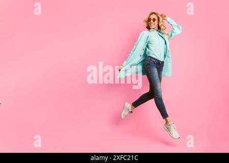 Donna con giacca blu salta davanti allo sfondo rosa Foto Stock