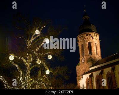 Scena notturna con una torre della chiesa illuminata e un albero decorato a festa in primo piano, kandel, germania Foto Stock