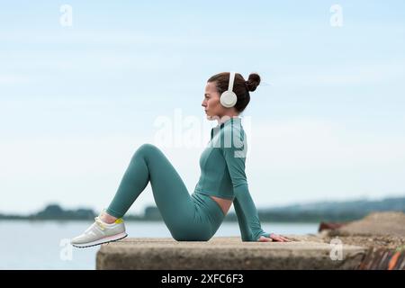 Donna sportiva seduta a riposare dopo l'allenamento con le cuffie Foto Stock