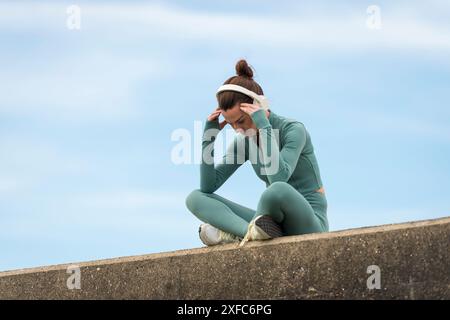 Donna sportiva seduta con la testa in mano e con le cuffie. concetto di motivazione. Foto Stock