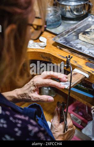 Le mani dell'artigiano modellano meticolosamente un gioiello con gli attrezzi Foto Stock