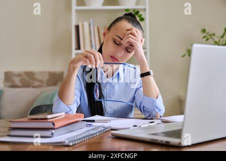 Una donna d'affari stanca che ha problemi a sedersi alla scrivania con un portatile Foto Stock