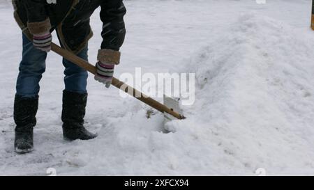 Il bidone pulisce la neve dalla pala. Il custode pulisce la strada dalla neve. Foto Stock