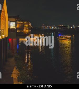 Giacarta, Indonesia - 11 maggio 2024. Una foto di una singola barca che naviga in una calma insenatura di notte. L'imbarcazione è illuminata da una luce calda che emette un leggero g Foto Stock