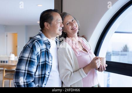 Una coppia di anziani sorride e si gusta un caffè mentre guarda fuori dalla finestra in vacanza Foto Stock