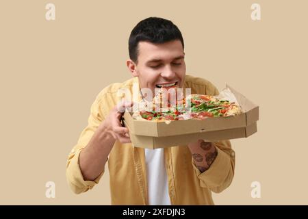 Giovane che mangia gustosa pizza su sfondo beige Foto Stock