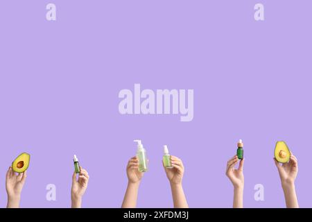 Mani femminili con avocado e bottiglie di prodotti cosmetici su sfondo lilla Foto Stock