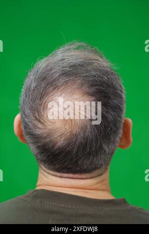 Un uomo con i capelli diradati sta in piedi con le spalle allo spettatore, su uno sfondo verde Foto Stock