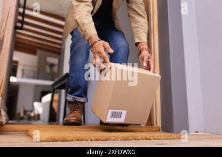 Consegna pacchi, uomo che ritira la scatola di cartone dalla porta di casa Foto Stock