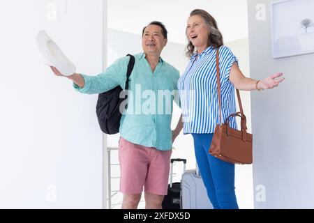 Una coppia anziana che arriva a casa per le vacanze, ha in mano i bagagli e sorride Foto Stock