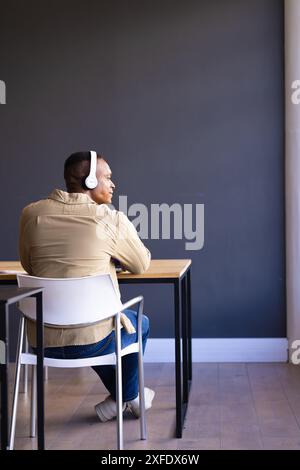 Indossa le cuffie, uomo seduto alla scrivania e distogliendo lo sguardo dall'ufficio, copia spazio Foto Stock