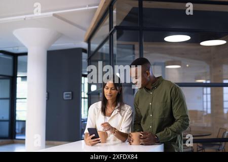 Discutere del lavoro, dei colleghi di lavoro che utilizzano lo smartphone e tengono le tazze da caffè in ufficio Foto Stock