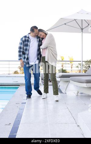 Una coppia senior che cammina accanto alla piscina, si gode la vacanza e si abbraccia a vicenda, copia spazio Foto Stock