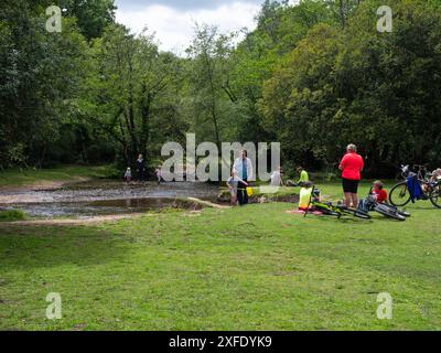 Ciclisti e persone accanto all'Avon Water Stream, di Wootton Copse, New Forest National Park, Hampshire, Inghilterra, Regno Unito, luglio 2020 Foto Stock