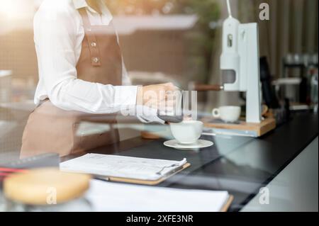 Immagine ravvicinata di una barista esperta che versa latte in una tazza da caffè, prepara gli ordini dei clienti e lavora in un bar. Foto Stock