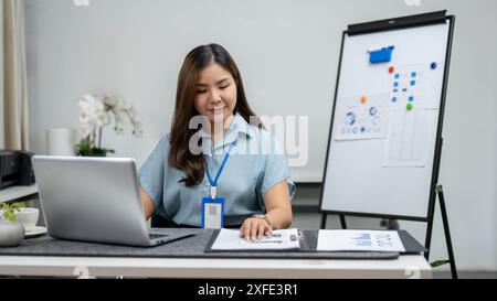 Una bella donna d'affari asiatica o una donna analista finanziaria lavora alla sua scrivania in ufficio, lavorando al suo computer e al suo direttore finanziario Foto Stock