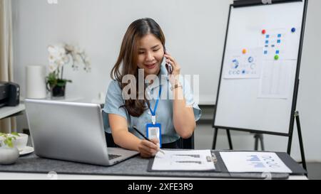 Una bella donna d'affari asiatica o un'impiegata sta rispondendo alla chiamata mentre lavora al rapporto alla sua scrivania. concetto di uomini d'affari Foto Stock
