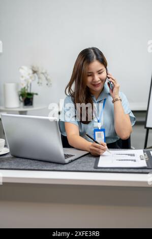 Una bella donna d'affari asiatica o un'impiegata sta rispondendo alla chiamata mentre lavora al rapporto alla sua scrivania. concetto di uomini d'affari Foto Stock