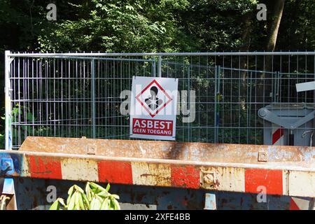 Traduzione: Asbest geen toegang - amianto senza accesso. Cantiere olandese con stoccaggio dell'amianto, contenitore per rifiuti, salto, cartello, recinzione. Estate, giugno Foto Stock