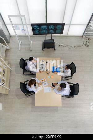 Gruppo di medici professionisti impegnati in una discussione o riunione in uno studio medico. Un monitor di grandi dimensioni che visualizza più scansioni cerebrali RM, per ruotare Foto Stock