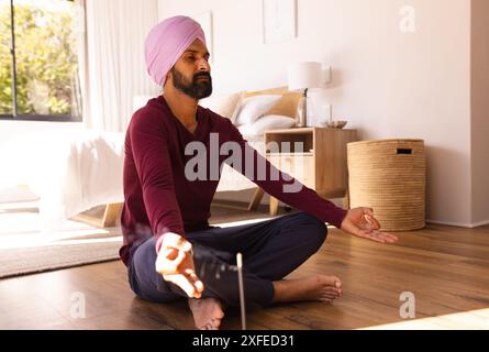 Meditando sul pavimento, uomo in turbante che pratica consapevolezza in camera da letto Foto Stock