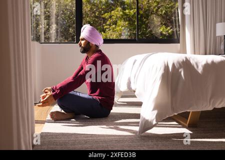 Meditare sul pavimento, uomo in turbante che pratica consapevolezza vicino a letto a casa, copiare spazio Foto Stock