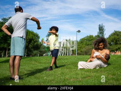 Famiglia latina in un parco, la madre allattando il bambino e il padre pugno bumping suo figlio Foto Stock
