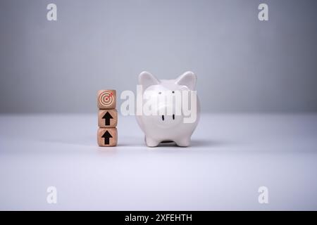 Salvadanaio e blocchi di legno con freccette e icone a freccia su di essi e sfondo bianco, risparmiando denaro e piano finanziario per il concetto di investimento, Bus Foto Stock