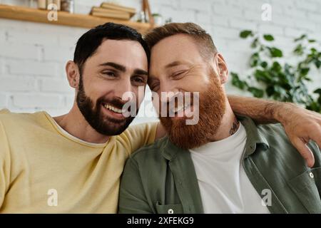 Due uomini, entrambi con la barba, si rilassano su un divano e si abbracciano a casa Foto Stock