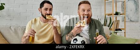 Due uomini con la barba si rilassano su un divano, mangiano pizza, bevono birra Foto Stock