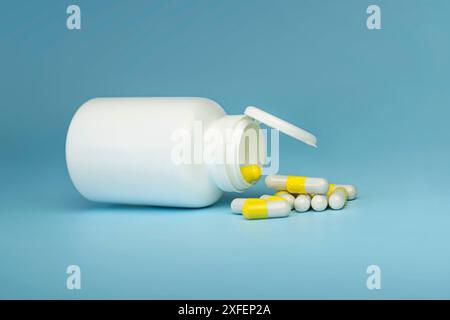 Immagine verticale del flacone di plastica bianco aperto e delle pillole di vitamine gialle su sfondo blu Foto Stock