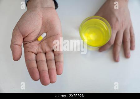 Le mani maschili tengono le piastre di pillole bianche e verdi e un bicchiere d'acqua su sfondo bianco. Concetto di trattamento. Vista dall'alto. Foto Stock