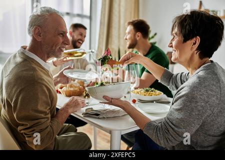 Una coppia gay si diverte a cenare con i genitori, mostrando un momento emozionante di accettazione familiare. Foto Stock