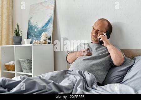 Un uomo con inclusività siede a letto a parlare al telefono. Foto Stock