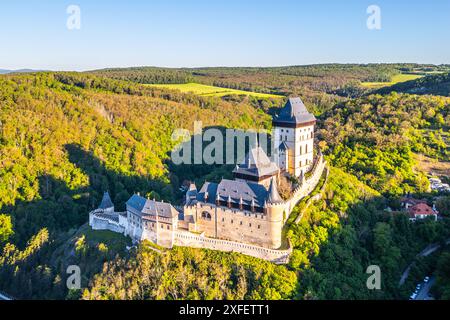 Prospettiva aerea del Castello di Karlstejn, immerso in un paesaggio boscoso con vegetazione lussureggiante in una giornata limpida e soleggiata in Cechia. Vista aerea dal drone. Foto Stock