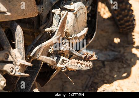 Un primo piano di una pedana per motociclette sporca e di un motore in una giornata di sole Foto Stock