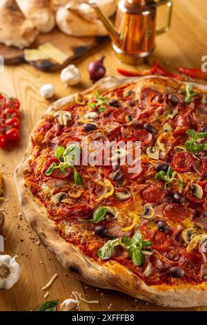 Appetitosa pizza al peperoni guarnita con basilico su sfondo di legno, circondata da ingredienti Foto Stock