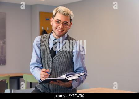 Ritratto di un giovane imprenditore latino attraente uomo al lavoro seduto sul tavolo, con un libro in mano, guardando la macchina fotografica e sorridendo, concetto di persone, copia Foto Stock